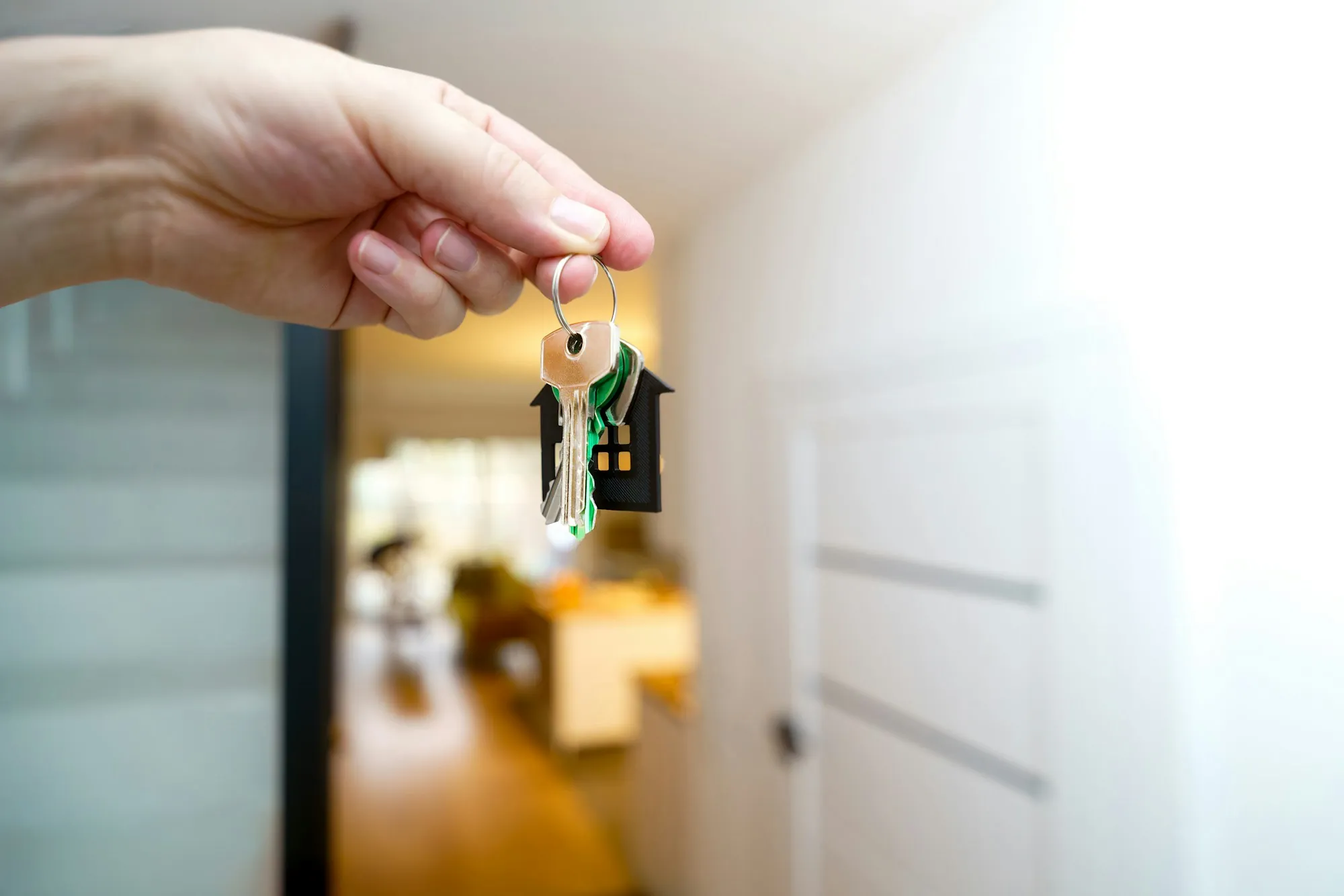 Hand holding keys with a house key chain in front of an open doorway